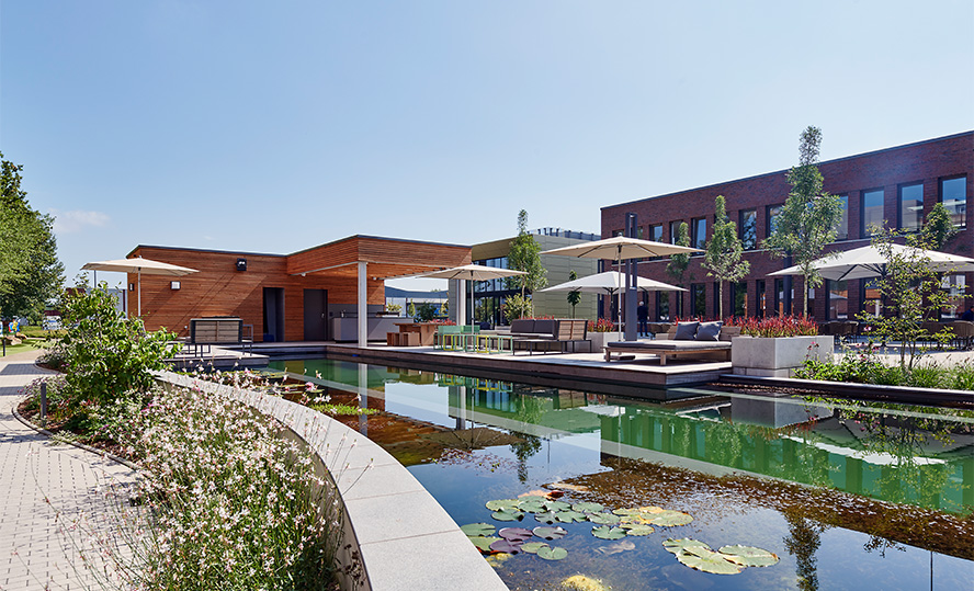 Weicon Gebäude von außen mit einem Naturteich, Sonnenschirmen und einer Terrasse im Sommer