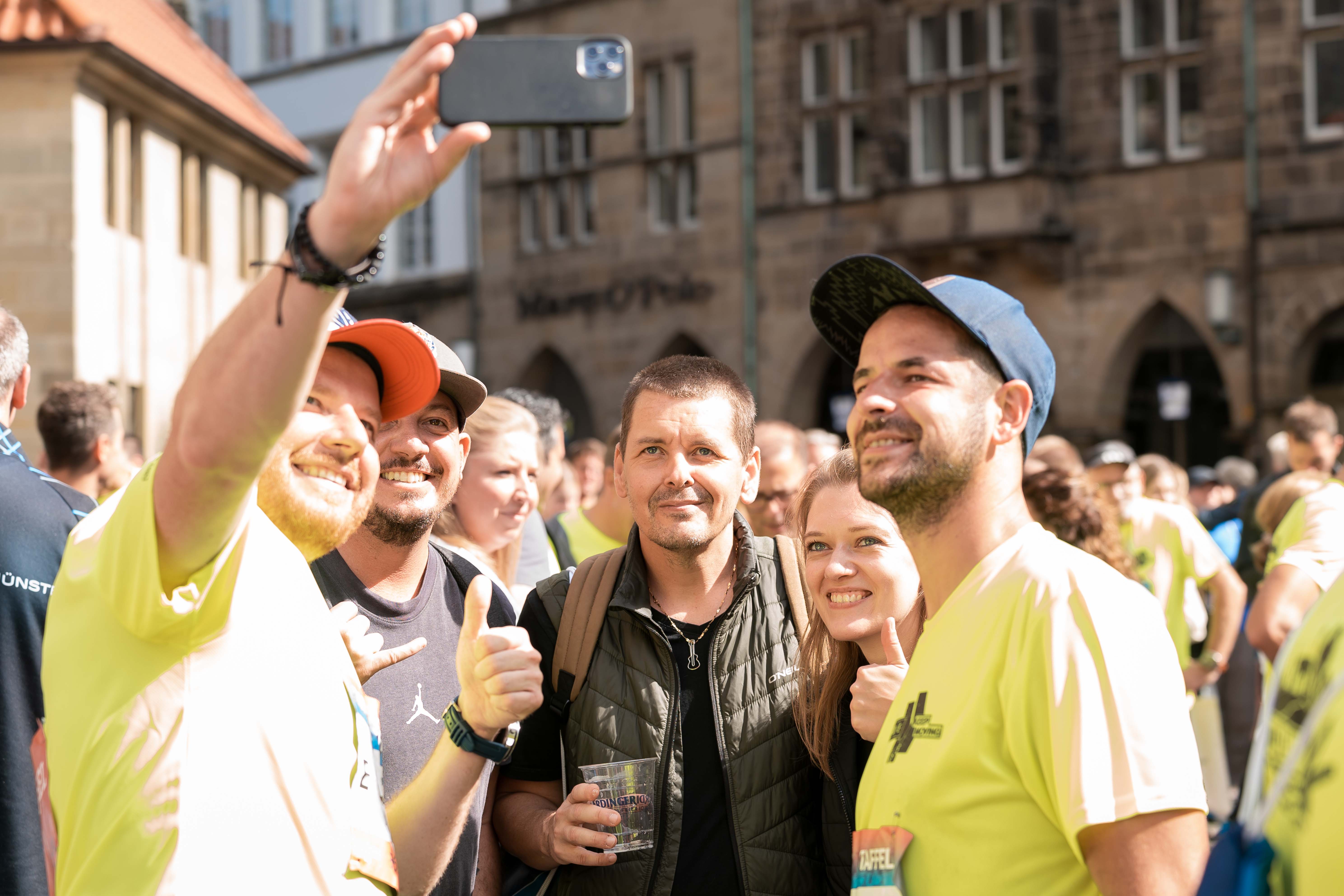 Fünf Personen stehen auf einem Platz und machen ein Selfie