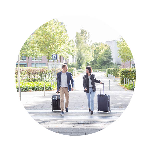 Ein Mann und eine Frau laufen mit jeweils einem Koffer in der Hand über einen Gehweg