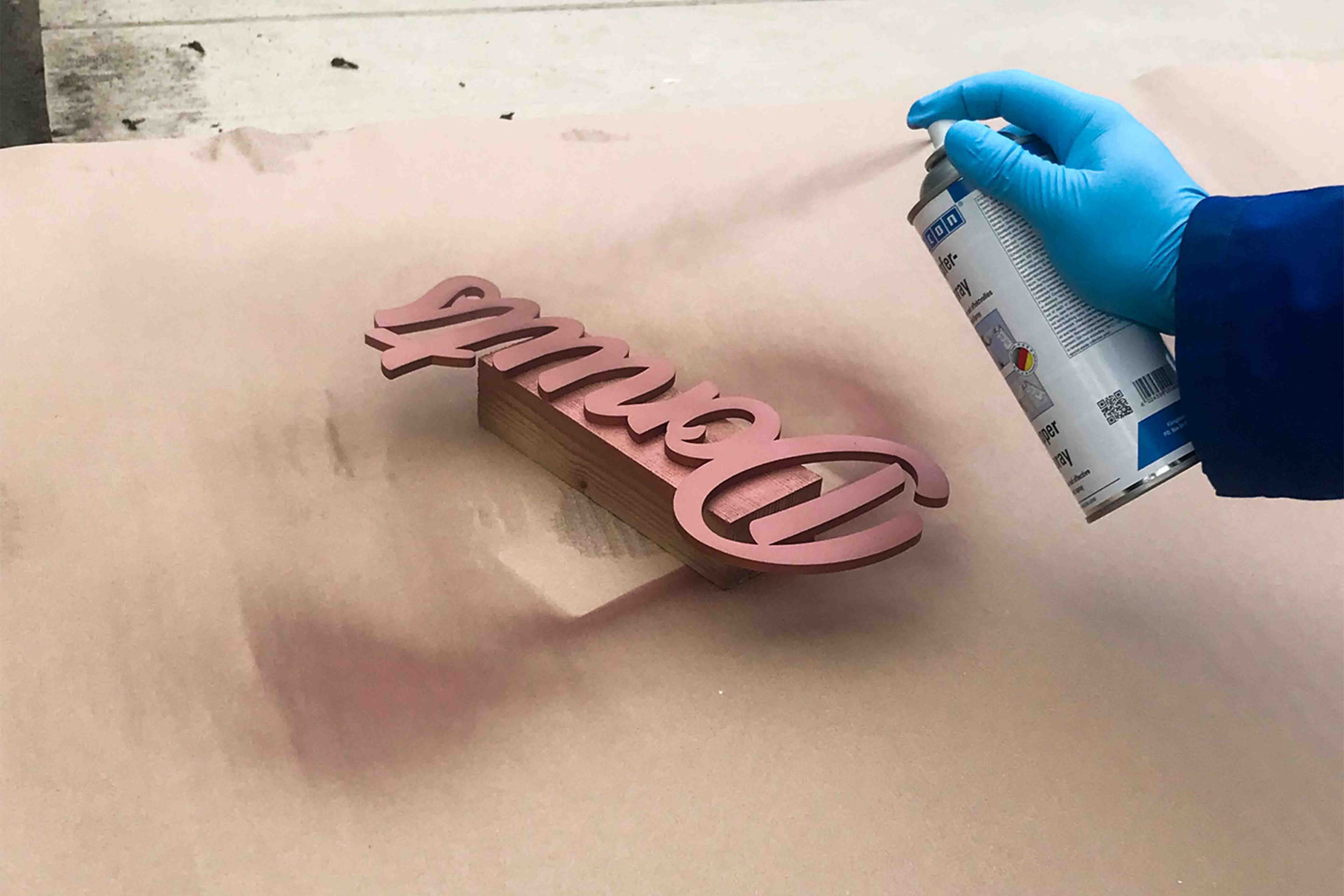 pink decor, wooden plaque, cutout word, spray painting, gloved hand
