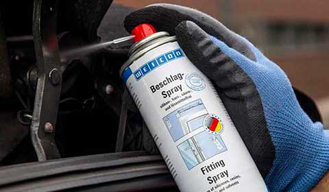 Weicon Beschlag-Spray wird auf den Hebel eines Türgelenks gesprüht