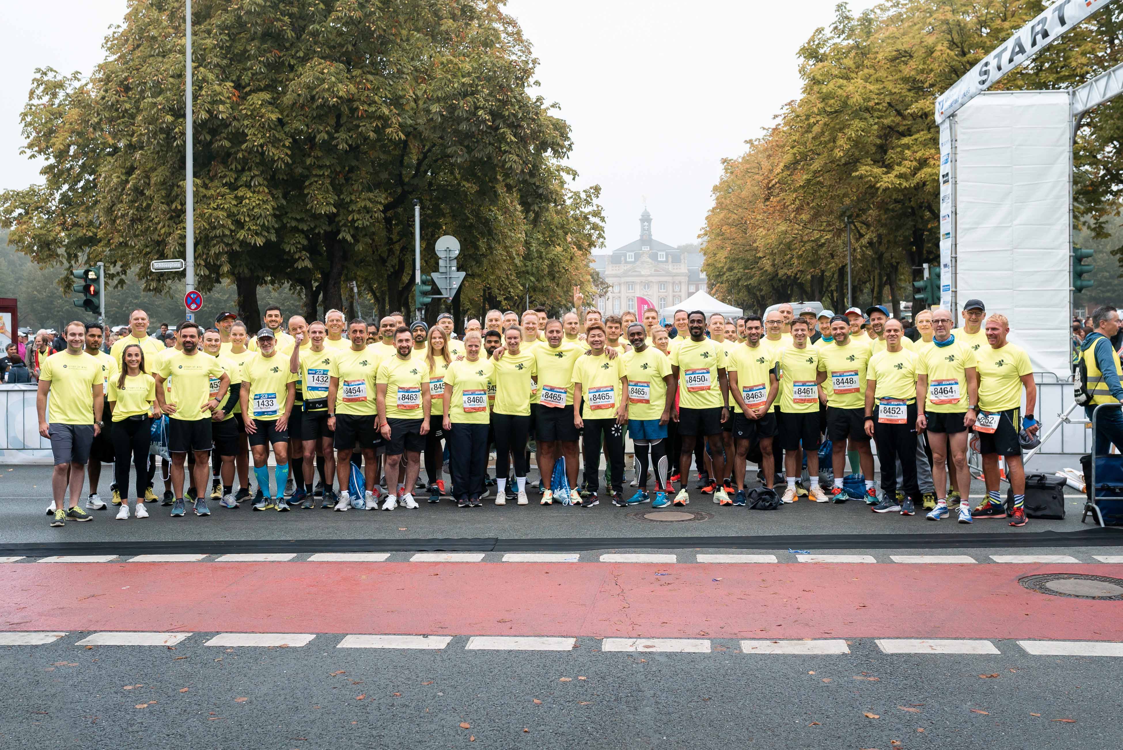 eine große Gruppe steht mit schwarzen Laufhosen und gelben Laufshirts auf der Straße