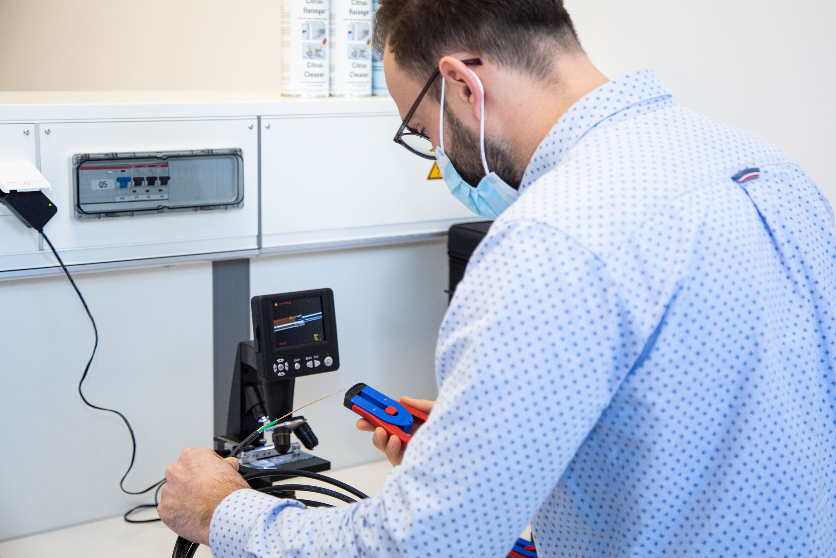 Ein Mann hat eine Maske auf und schaut sich ein Abisolierwerkzeug an