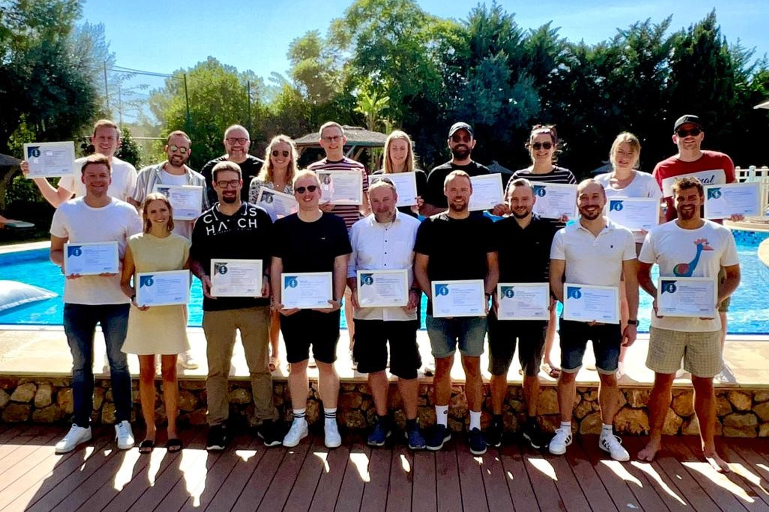 eine Gruppe steht im Sommer vor einem Pool und hält Zertifikate in der Hand