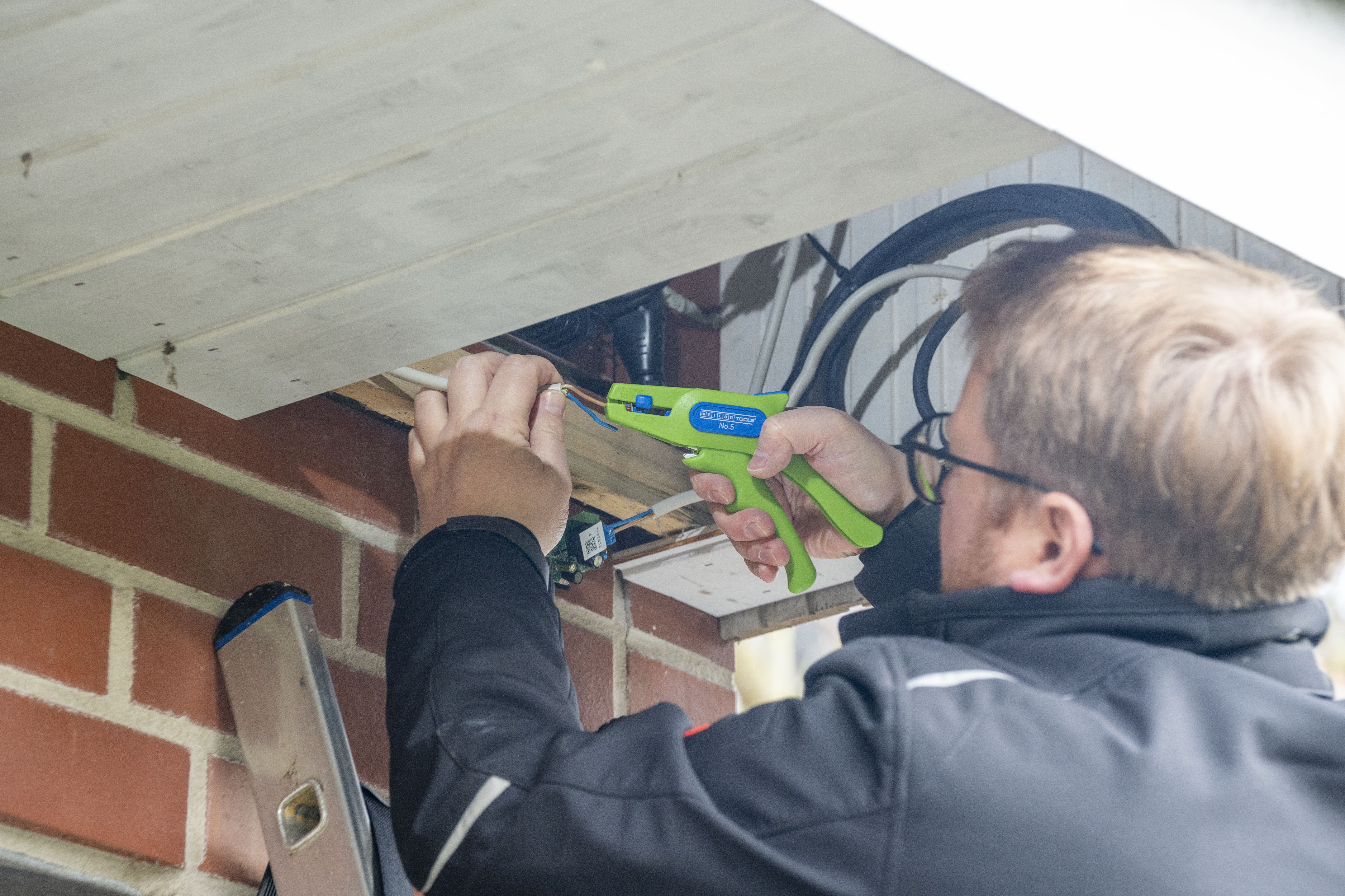 Ein Mann isoliert an einer Hauswand ein Kabel mit der Green Line Abisolierzange No. 5 ab