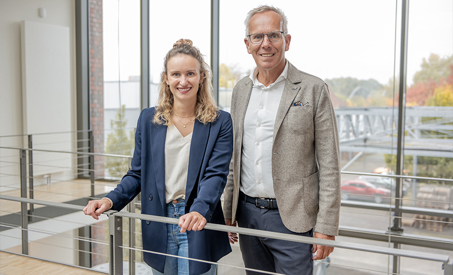 Ralph und Ann-Katrin Weidling stehen an einem Geländer im Gebäude und lachen in die Kamera