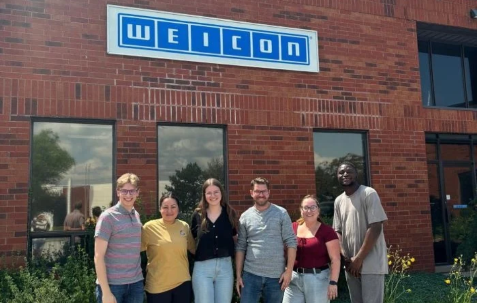 group photo, brick building, welcome sign, outdoor, people