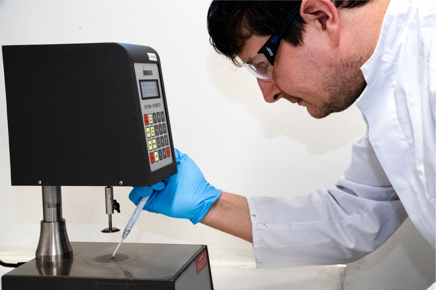 Ein Mann mit weißem Kittel gibt etwas aus einer Pipette auf eine Oberfläche