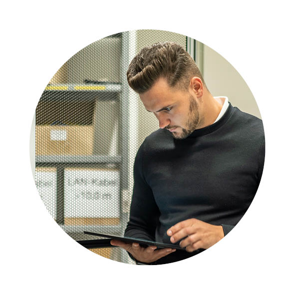 Ein Mann steht vor einem Schaltschrank und schaut auf sein Tablet