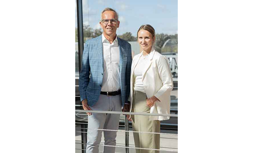 Ralph und Ann-Katrin Weidling stehen an einem Geländer im Gebäude und lachen in die Kamera