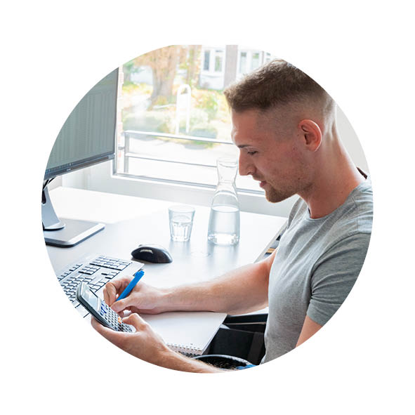 Ein Mann sitzt im Büro am Schreibtisch und tippt etwas in den Taschenrechner